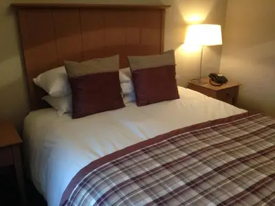 a bedroom with a large bed with white sheets and pillows at Dumfries Arms Hotel in Cumnock