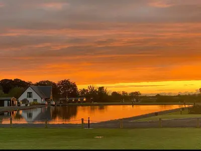 a sunset over a body of water with a house at Arranview Lochside Pods & Lodges all with private Hot-tubs in Fenwick
