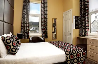 a bedroom with a bed and a desk and a window at SGE Esplanade Hotel in Dunoon