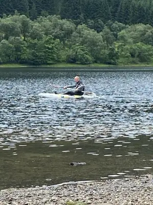 a man sitting in a kayak on a lake at Pine Cabin, Strathyre. A cosy escape from it all. in Strathyre