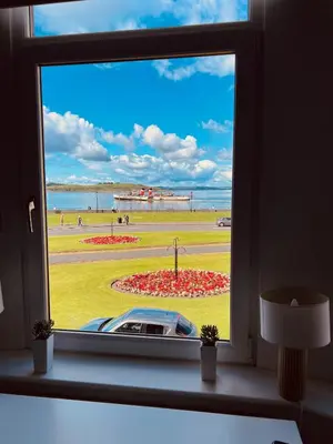 a window with a view of a beach and a car at Seaview one bedroom apartment in centre of Largs in Largs