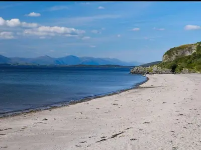 a beach with the ocean and mountains in the background at Machrie Cottage, Oban, in Oban