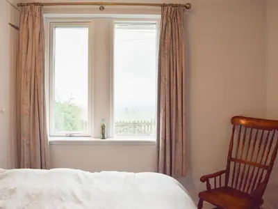 a bedroom with a bed and a chair and a window at Puddingstone Cottage in Gartmore