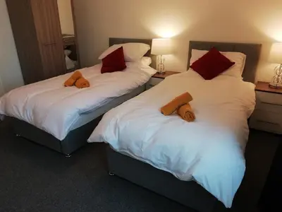 two beds in a room with white sheets and red pillows at Carvetii - Vincent House - Large 3 bedroom apartment with on-site parking in Fife