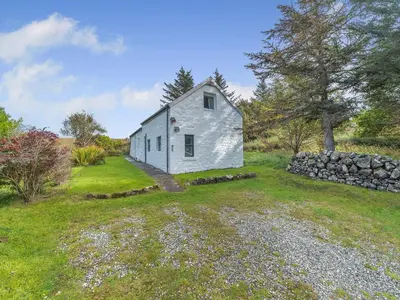 a white house in a field with a stone wall at The Bothy - Uk37414 in Bunessan
