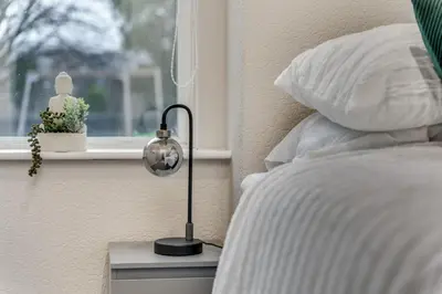 a bed with a lamp on a night stand next to a window at The Garden Flat, Loch Lomond in Alexandria