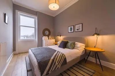 a bedroom with a bed with a table and a window at The Trossachs Apartment in Doune