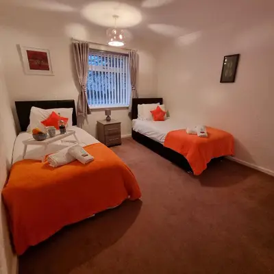 two beds in a room with orange sheets at PREMIER - Whifflet Apartment in Coatbridge