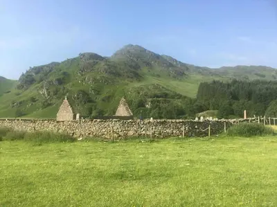 a stone wall in a field with a mountain at The Den - your cosy sleepover space in Saint Fillans