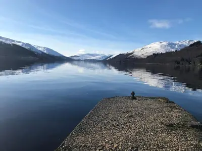a person sitting on the edge of a body of water at The Den - your cosy sleepover space in Saint Fillans