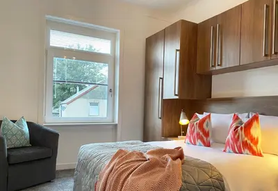 a bedroom with a bed and a chair and a window at Gladsmuir House in Glasgow