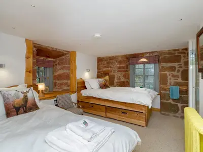 a bedroom with two beds and a stone wall at Knock Old Castle in Largs