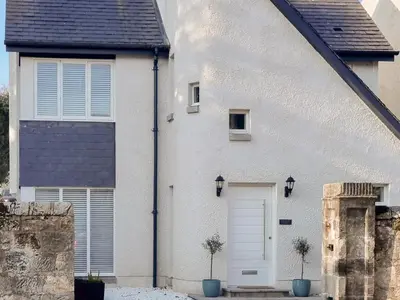 a white house with a door and two potted plants at Forget Me Not Cottage in Culross