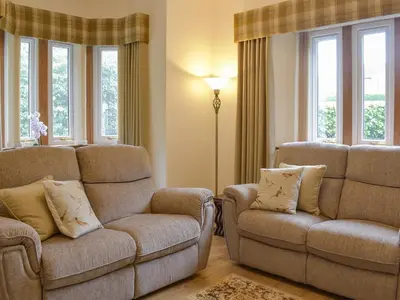 a living room with a couch and a chair and windows at The Lodge in Linlithgow