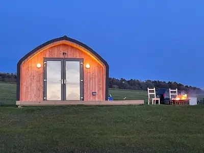 a wooden barn in a field with a grill at Fox's Den in Bathgate