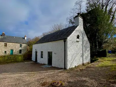 a white building with a black roof next to a house at The Bothy of Ballachulish House in Ballachulish