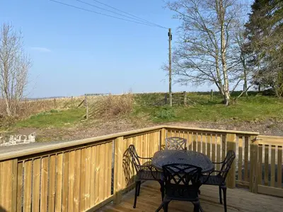 a table and chairs sitting on a wooden deck at Partridge Lodge with Hot Tub in Forgandenny