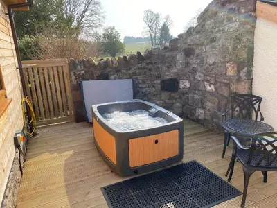 a hot tub sitting on a deck with a table at Pheasant Lodge with Hot Tub in Forgandenny