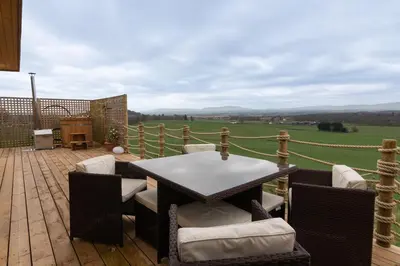 a patio with a table and chairs on a wooden deck at The Paddock- Loch Lomond and Trossachs in Gartmore