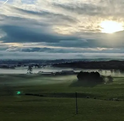 a foggy field with the sun in the background with the sun rising at The Paddock- Loch Lomond and Trossachs in Gartmore