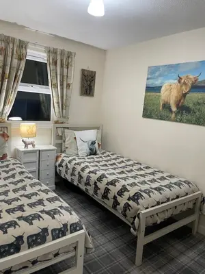 a bedroom with two beds and a cow painting on the wall at Lamlash (holiday) Lets in Lamlash