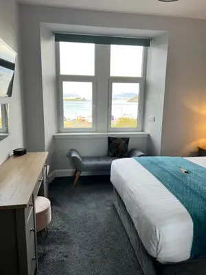 a bedroom with a bed and a bench and two windows at Killorn Guest House in Oban