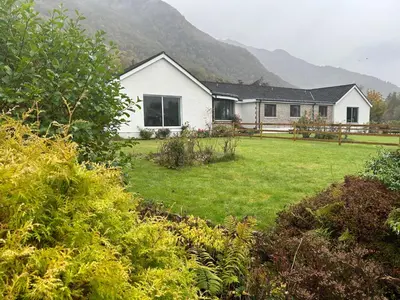 a white house with a yard in front of a mountain at Lyn leven cottages in Ballachulish