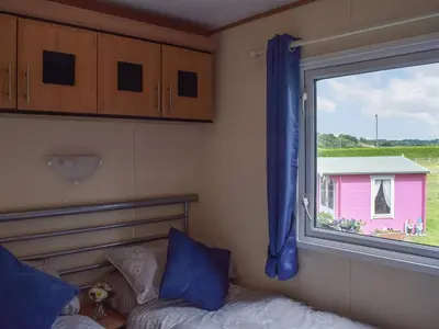 a bedroom with a window and a bed and a pink house at Tranquillity Lodge in Annbank
