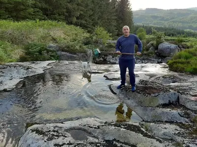 a man standing on rocks with a stick in a stream at 1 Bed Cabin in the Magical Galloway Forest Park in Newton Stewart