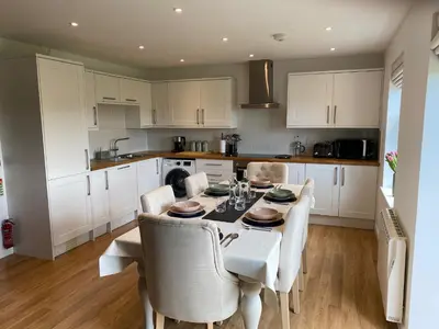a kitchen with white cabinets and a table and chairs at No 2 The Cairns, Unwind in Style in Oban
