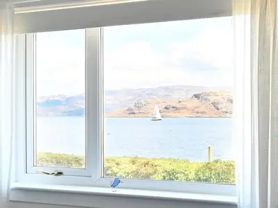 a window with a view of a sailboat in the water at Taigh An Uillt in Tighnabruaich