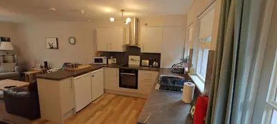 a kitchen with white cabinets and a living room at Ben Reoch Cottage - Loch Lomond and Arrochar Alps in Tarbet