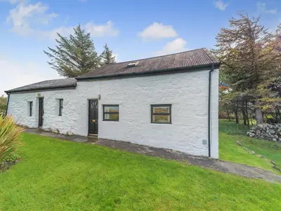 a white building with a door on a grass field at The Stables - Uk37415 in Bunessan