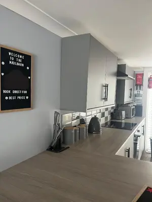 a kitchen with white cabinets and a sign on the wall at The Mail Barn in Lamlash