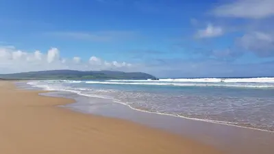 a sandy beach with waves in the ocean at Ronachan in Clachan