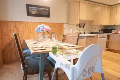 a kitchen with a table with chairs and flowers on it at Steading Cottage - 50m from the beach in Port Appin