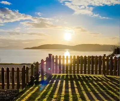 a fence with the sun setting over the water at Craigneuk near Oban, stunning home with sea views in Oban