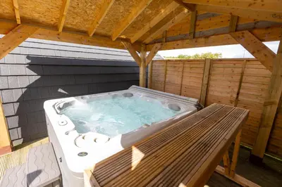 a hot tub on a deck with a wooden roof at Fulshaw Mill Holidays in Stewarton