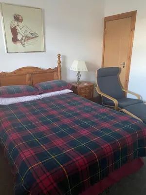 a bed with a plaid blanket and a chair in a room at Rooms at Tarrareoch in Bathgate