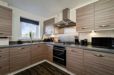 a kitchen with wooden cabinets and a stove top oven at Modern 3-Bed Family Home Near Glasgow Airport in Bishopton
