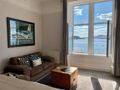 a living room with a couch and a large window at Westbay Seafront Apartment in Oban
