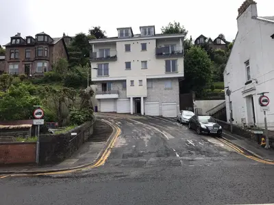 an empty street with a white house and cars parked at Beautiful 3-Bed Apartment in Gourock in Gourock