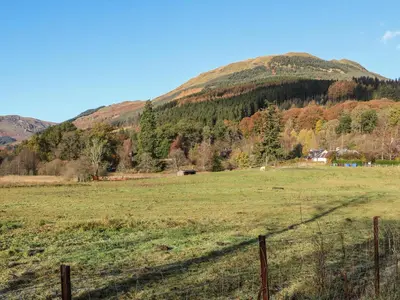 a field with a fence in front of a mountain at Inglis Nook Cottage in Lochearnhead