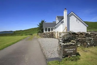 a house with a stone wall next to a road at Ardlarach Lodge in Cullipool