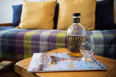 a bottle of alcohol sitting on a table with a book and a glass at Gaidrew Cottage in Drymen