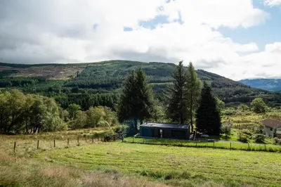 a small house in a field with mountains in the background at Am Bothan in Lochearnhead
