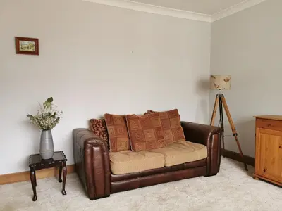 a brown leather couch sitting in a living room at Arrochar Fern Cottage with Wood Burner & Loch View in Arrochar
