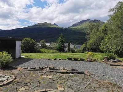 a backyard with a stone patio with mountains in the background at Arrochar Fern Cottage with Wood Burner & Loch View in Arrochar
