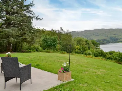 a patio with a table and chairs and a field of grass at Boatman's Cottage At Invernian Mor in Inverinan Beg