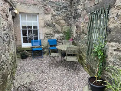 a patio with chairs and a table in a stone wall at Arden House in Comrie